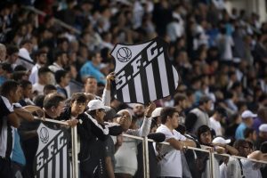 Torcedores do Santos na arquibancada segurando placa que reproduz escudo do clube