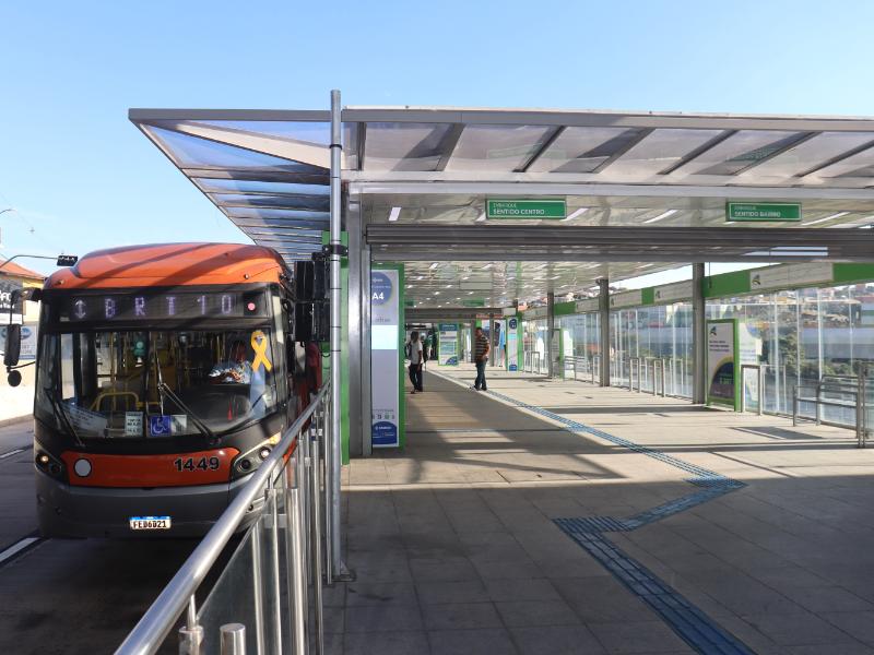 Ônibus laranja estacionado em plataforma de estação com estrutura de cobertura e painéis de orientação, em Campinas, enquanto as obras do BRT em Campinas indicam interdição do trecho com início das intervenções.