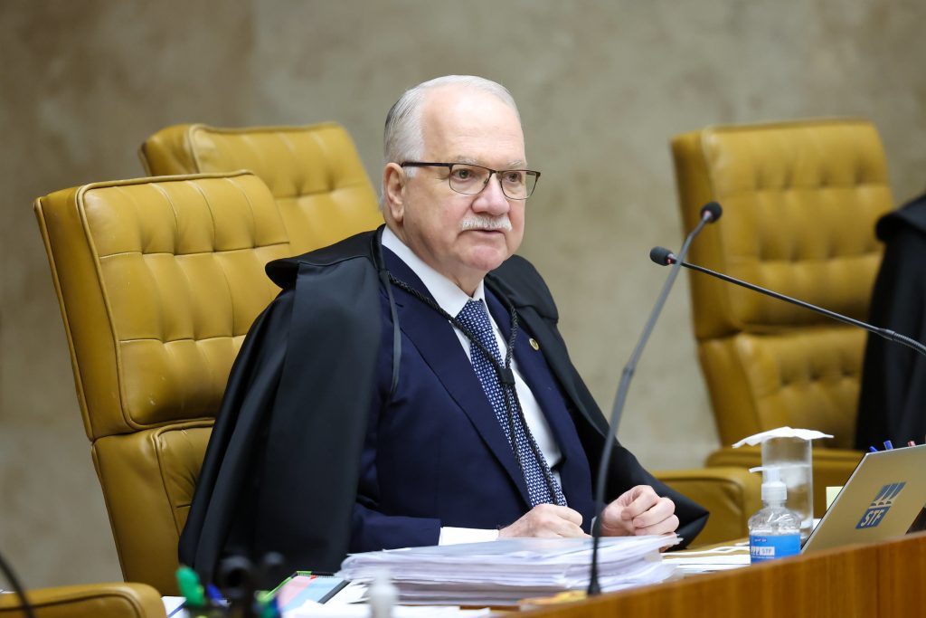 STF visto: Ministro Edson Fachin, do STF, em sessão no plenário, usando toga e falando ao lado de microfones, com cadeiras amarelas ao fundo.
