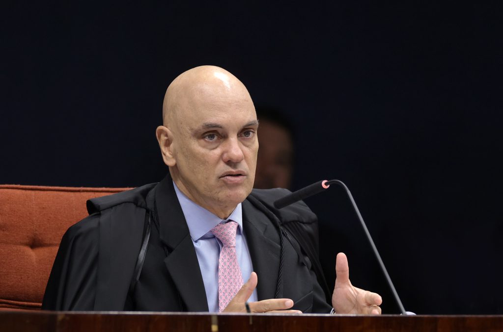 Julgador Alexandre de Moraes em sessão no STF, sentado em cadeira laranja e falando ao microfone, com expressão séria e gesto com a mão; foto Rosinei Coutinho/STF.