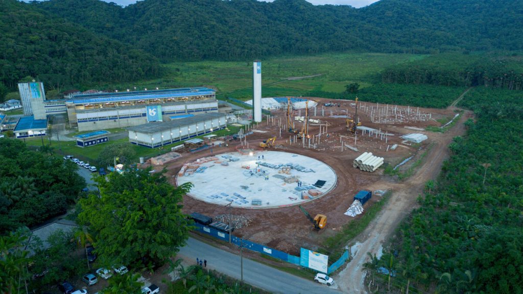 Vista aérea de obras e estruturas de uma estação de tratamento de água em canteiro industrial, com áreas em construção e movimentação de equipamentos, tema relacionado aos investimentos da Sabesp na Baixada Santista.