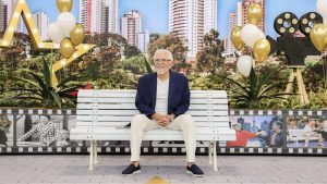 Carlos Alberto de Nóbrega sorridente no banco do programa A Praça É Nossa do SBT celebrando 90 anos.