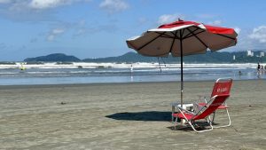 Voluntários em mutirão de limpeza na praia do Gonzaga, Santos, recolhendo bitucas de cigarro e lixo.