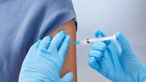 Enfermeira aplicando vacinação contra a gripe em paciente idoso em Unidade Básica de Saúde.