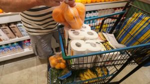 Carrinho de supermercado com alimentos e cédulas de Real, representando a inflação de março e o custo de vida.