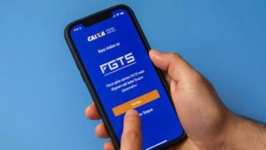 Trabalhador utilizando smartphone para consultar o saldo do FGTS e informações sobre o Saque-Aniversário e o programa Desenrola 2.0 no aplicativo da Caixa.