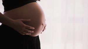 Imagem em tons suaves com gestante de mãos sobre a barriga, destacando o tema justa causa de grávida, com contexto de decisão judicial sobre afastamento prolongado por mais de 70 dias.