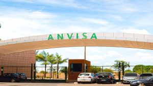 Fachada do prédio da ANVISA com o letreiro “ANVISA” ao fundo e carros em frente ao órgão regulador. Imagem relacionada à decisão sobre lotes e risco à segurança do consumidor.