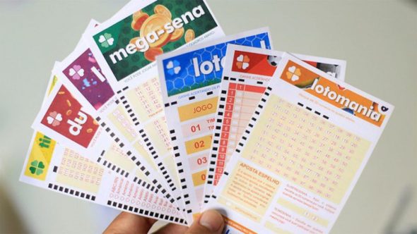 Cartelas e jogos de loterias da Caixa com apostas impressas em destaque, incluindo Mega-Sena, Lotofácil, Dupla-Sena e Joromonia, em mãos, com fundo claro.