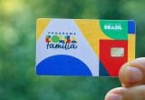 Documentos Bolsa Família em uma imagem com cartão do Programa Família Brasil, símbolo do Brasil, sendo segurado por uma mão diante de fundo verde.