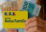 pagamentos de benefícios em Agosto: Mão segurando cartão do programa Bolsa Família ao lado de cédulas de dinheiro, com mensagem sobre benefícios pagos em agosto. Benefícios podem somar mais de R$ 1 mil.