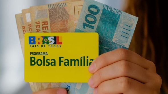 pagamentos de benefícios em Agosto: Mão segurando cartão do programa Bolsa Família ao lado de cédulas de dinheiro, com mensagem sobre benefícios pagos em agosto. Benefícios podem somar mais de R$ 1 mil.