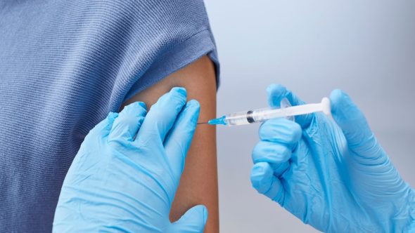 Enfermeira aplicando vacinação contra a gripe em paciente idoso em Unidade Básica de Saúde.