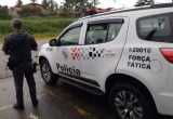 Homem baleado na cabeça em São Vicente: equipe de Força Tática ao lado de uma viatura da Polícia, com um policial em pé na rua e o veículo ao fundo, em área urbana.