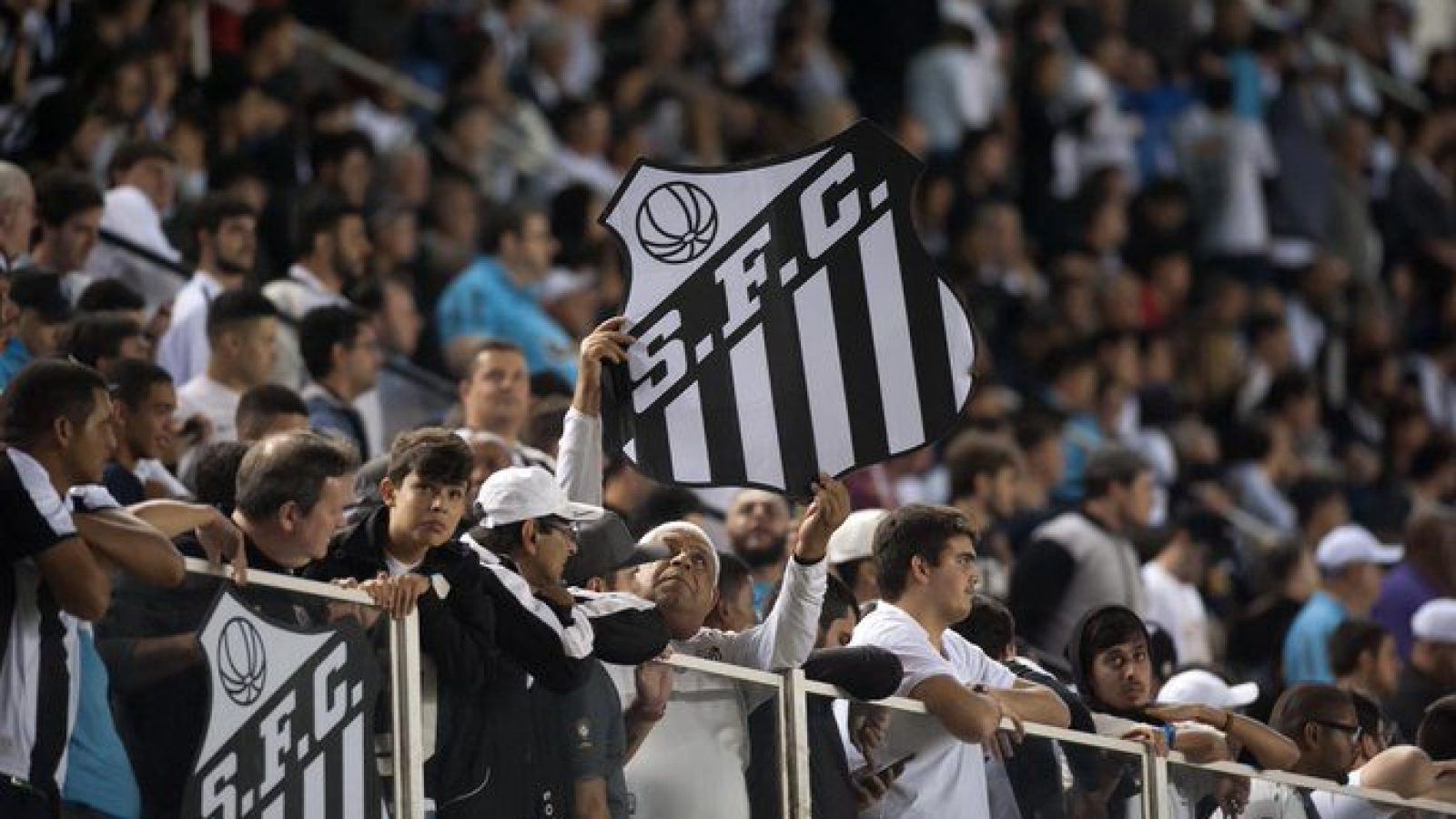 Torcedores do Santos na arquibancada segurando placa que reproduz escudo do clube