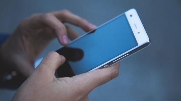 Celulares roubados: pessoas segurando um smartphone azul em ambiente escuro, ilustrando o tema de como criminosos alteram o IMEI e desbloqueiam aparelhos