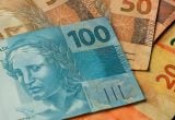 Imagem com cédulas de dinheiro do Brasil, com destaque para notas de 100 reais e outras cédulas, simbolizando pagamento do PIS/Pasep e abono salarial.
