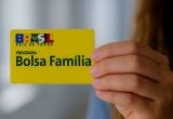 Beneficiária segurando cartão do Bolsa Família para saque do pagamento de março em agência bancária.