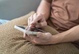 Pessoa em casa com um celular nas mãos, enquanto uma mensagem de apoio do SUS destaca o tema vício em bets e a previsão de 100 mil atendimentos.