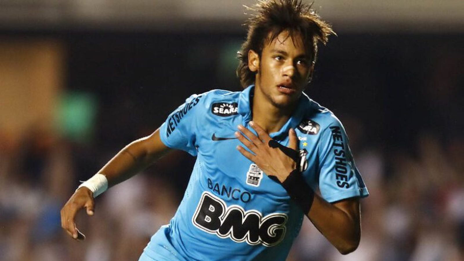 Neymar em sua 1ª passagem pelo Santos, vestindo o uniforme azul de 2012, comemora gol batendo no peito.