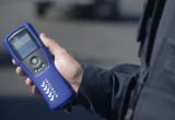Imagem mostra uma pessoa segurando um bafômetro digital azul, em fiscalização ao lado de um veículo. Contran altera Lei Seca para incluir teste de drogas e novo bafômetro.