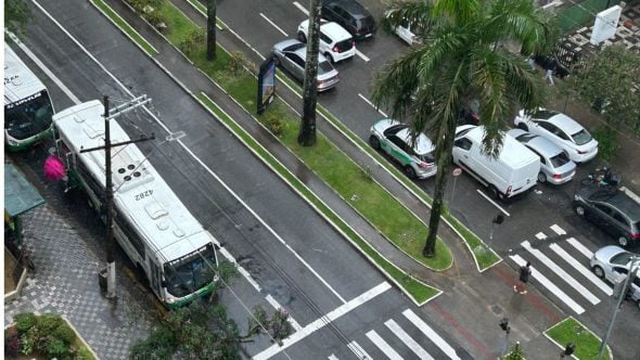 Movimentação de trânsito em avenida urbana com carros e ônibus em São Paulo, imagem que ilustra a previsão do tempo em São Paulo com temperaturas mais baixas e possibilidade de chuva no litoral no fim de semana.