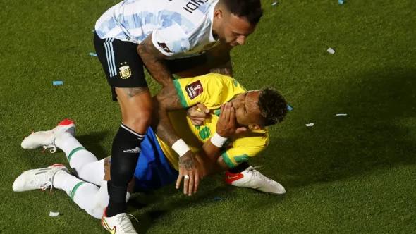 Raphinha é levantado por Otamendi depois de tomar cotovelada na boca, em jogo entre Brasil e Argentina