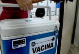 Caixa térmica de vacina com o texto “VACINA”, em um ambiente de campanha de saúde, destacando a necessidade de prevenção e atenção às mortes por gripe em Campinas