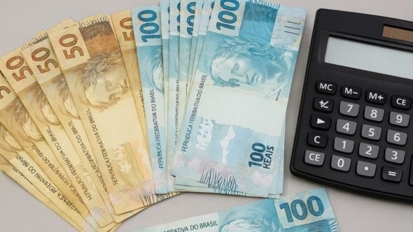 Cartões de cédulas de dinheiro brasileiro de R$ 100 e um calculadora ao lado, imagem que ilustra quanto rende R$ 260 milhões do prêmio da Quina de São João e possibilidades de uso do dinheiro.