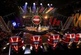 The Voice Brasil apresenta novo time de técnicos para a temporada 2026 em um palco de reality show com jurados em cadeiras vermelhas e público ao fundo, luzes e telões no cenário.